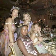 four women in dresses sitting at a table with wine glasses and candles on top of it