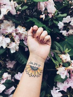 a woman's arm with a sunflower tattoo on it and flowers in the background