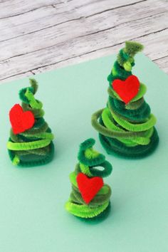 three felt christmas trees sitting on top of a piece of green paper next to a red heart