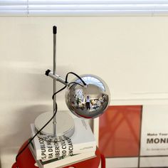 a chrome ball sitting on top of a red table next to a stack of books