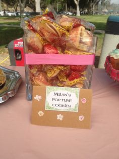 there is a pink table with many pastries in plastic containers on it and a sign that says man's fortune cookies