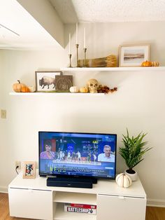 a flat screen tv sitting on top of a white entertainment center next to a potted plant