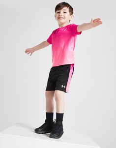 a young boy in pink shirt and black shorts standing on top of a white block