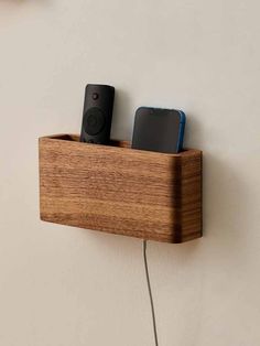 two remotes are plugged into a wooden charging station on the wall, one is connected to a smart phone