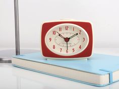 a red and white alarm clock sitting on top of a blue book next to a lamp