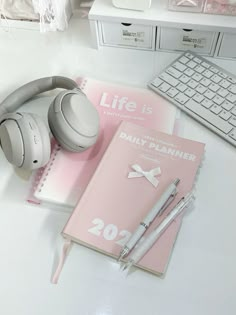 a notebook, pen and headphones sitting on top of a desk next to a keyboard