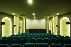 an empty theater with rows of blue chairs and projector screen on the wall,