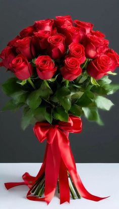 a bouquet of red roses in a vase with a ribbon tied around the top and bottom