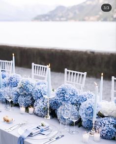 the table is set with blue flowers and white candles for an elegant wedding reception by the water