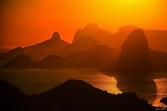 the sun is setting over an island with mountains in the foreground and water on the far side