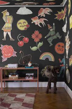 a black dog standing in front of a wall covered with cartoon images