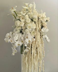 white flowers are arranged in a vase with long strands hanging from the top and bottom