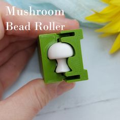 a hand holding a green and white mushroom bead roller with yellow flowers in the background