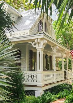 a white house with an american flag on the porch and palm trees in front of it