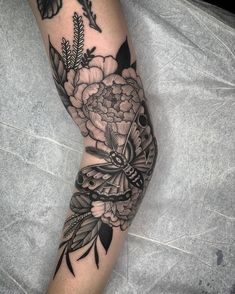 a woman's arm with flowers and a butterfly tattoo on her left forearm, in black and grey