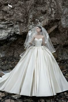 a woman wearing a wedding dress and veil standing on rocks in front of a cliff