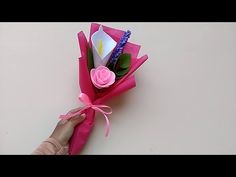 someone is holding a pink paper flower with purple and white flowers in it on a table