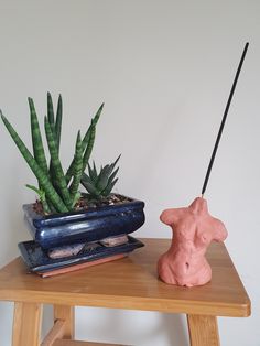 a small pink sculpture sitting on top of a wooden table next to a potted plant