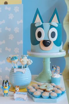 a blue and white cake sitting on top of a table next to cupcakes