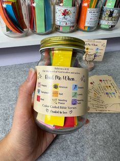 a hand holding a jar filled with lots of colored pencils next to some cards