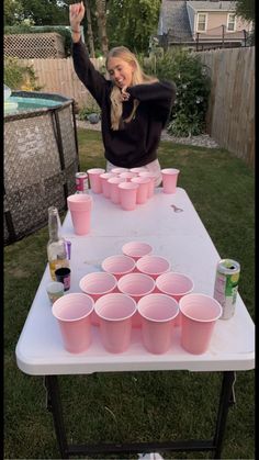 a woman standing at a table with cups on it and her hand up in the air