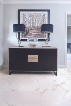 a black and gold sideboard with two lamps on it in front of a painting