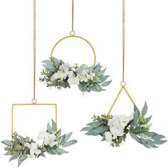 two white flowers and greenery are hanging from gold geometric frames with golden bars on them