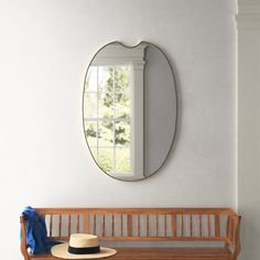 a wooden bench with a hat on it in front of a round mirror and window