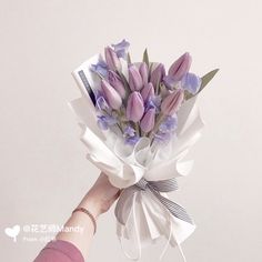 a hand holding a bouquet of purple tulips and lavender flowers on a white background