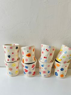 five cups are lined up on the table and one is painted with different colors, shapes and sizes