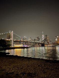 the city skyline is lit up at night with lights reflecting on the water and bridge in the foreground