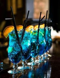 several glasses filled with blue liquid and garnished with lemon wedges on a bar