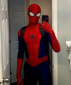 a man in a spiderman costume taking a selfie with his cell phone while standing in front of the door