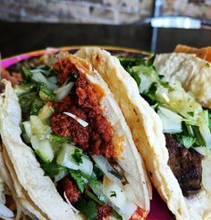 three tacos with meat, lettuce and other toppings on a plate