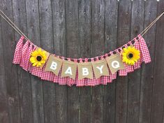 a baby shower banner with sunflowers hanging from it's side on a fence