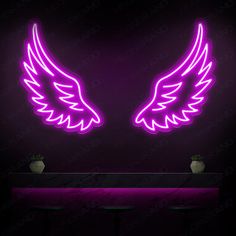 two neon angel wings sitting on top of a table in front of a black wall