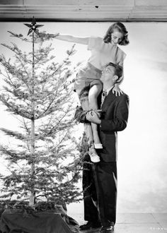 a man holding a child on his shoulders next to a small christmas tree in front of him