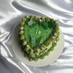 a heart shaped cake with green frosting and butterflies on it, sitting on a white plate