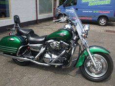 a green motorcycle is parked in front of a building with a blue van behind it