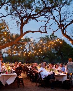 an outdoor dining area with tables and people sitting at them, surrounded by string lights