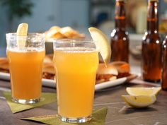 two glasses filled with orange juice sitting on top of a table next to plates of food