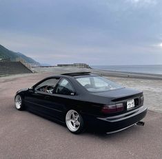 a black car parked on the side of a road next to the ocean and steps