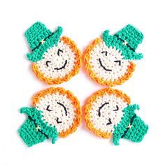 four crocheted shamrock coasters with smiling faces on them, all in green and orange