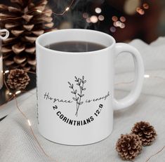 a white coffee mug sitting on top of a table next to pine cones and candles