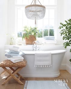 a white bath tub sitting under a window next to a rug and potted plant