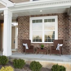 two chairs sitting on the front porch of a brick house with white trim and windows