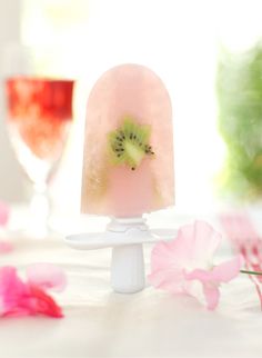 a popsicle with kiwi slices on it sitting next to two glasses of wine