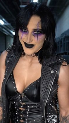 a woman with black makeup and piercings on her face wearing a leather outfit in a warehouse