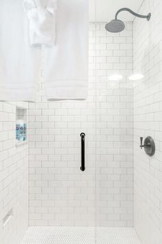 a white tiled shower with black handles and hand held faucet in the corner