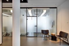 two chairs and a table in front of a glass wall with an open door on the other side